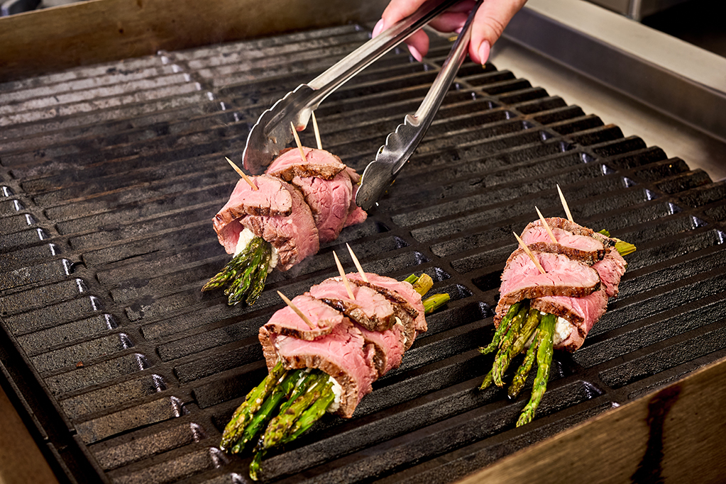 Placing steak-wrapped asparagus onto the grill