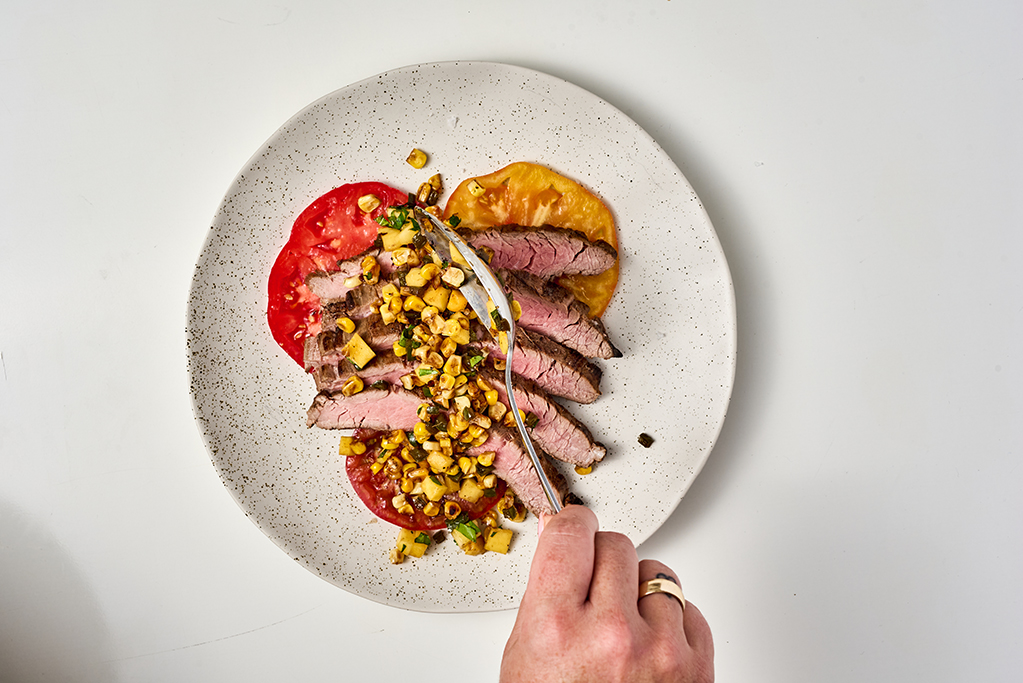 Spooning relish over steak and tomato dish